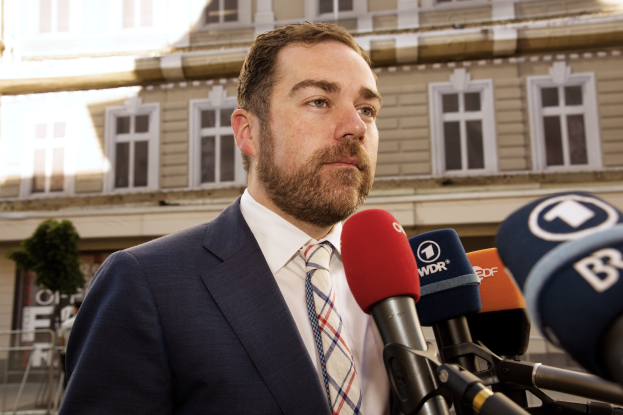 Ein Mann im Anzug und Krawatte steht vor Mikrofonen und spricht zur Presse vor einem Gebäude, wahrscheinlich wegen seiner dreijährigen Haftstrafe.