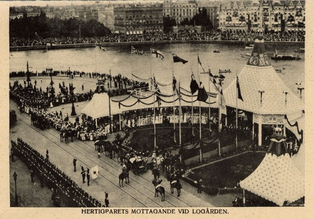 Ein altes Schwarz-Weiß-Foto einer Menschenmenge, die sich um einen Karneval mit Zelten, Fahnen, Stangen und Pferden im Vordergrund und Gebäuden, Bäumen und Wasser im Hintergrund versammelt hat, mit Text am unteren Rand des Bildes.