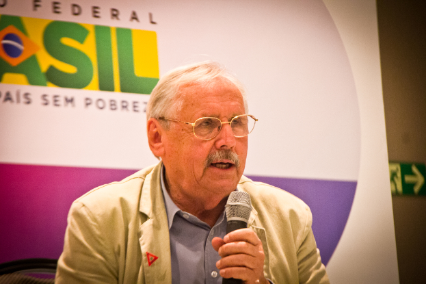 Eine Person, die in ein Mikrofon spricht und im Hintergrund ein Banner mit der Aufschrift 'Bundes' sieht.