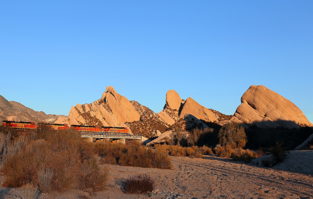Ein Zug auf einer Brücke mit Klippen und Pflanzen im Hintergrund.