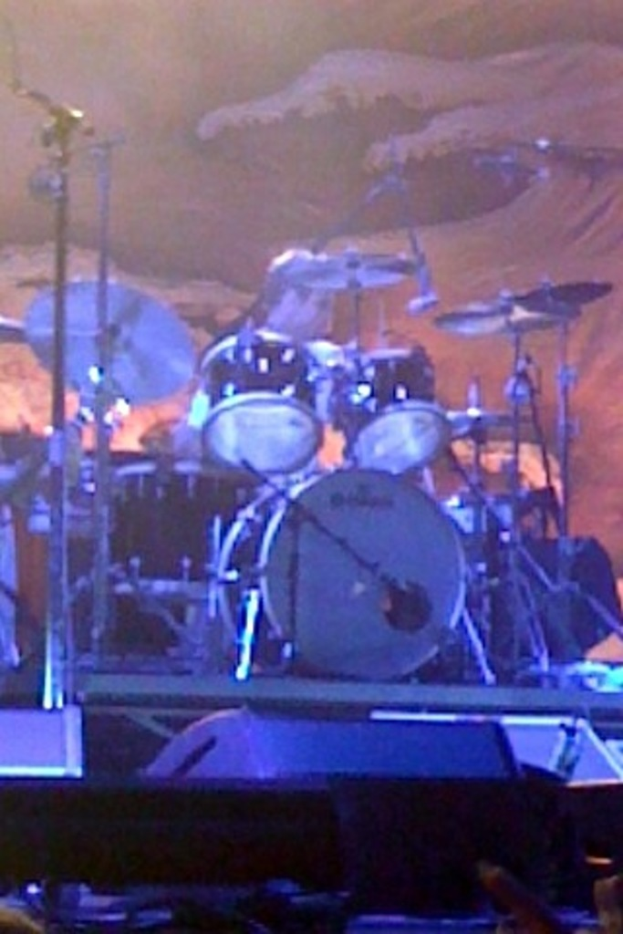 Eine Person sitzt hinter einem Drumset mit verschiedenen Drogen davor.