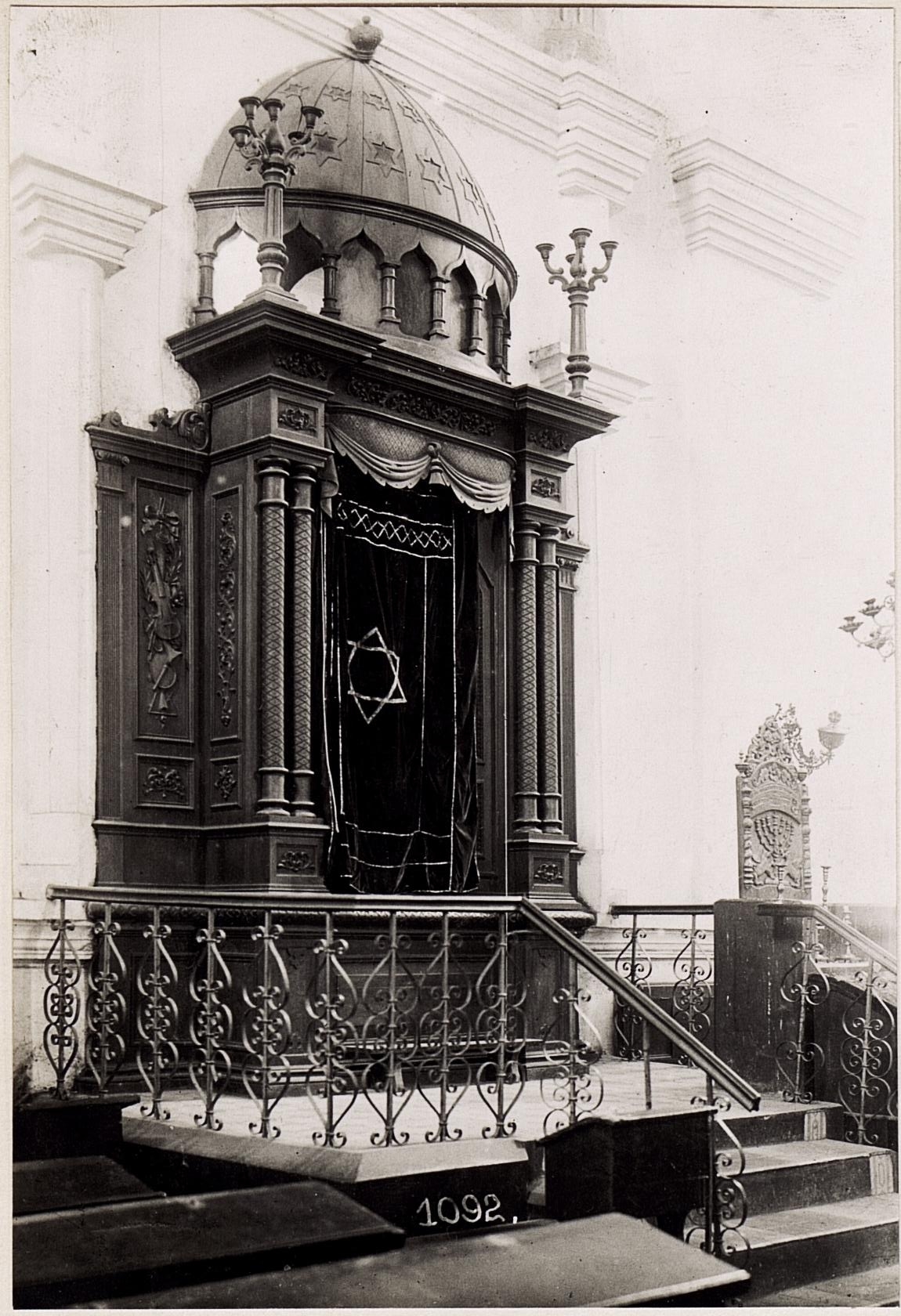 Ein altes Schwarz-Weiß-Foto einer jüdischen Synagoge in New York City, das eine Treppe, Geländer, Säulen, eine Tür und eine Wand zeigt, mit einem Text am unteren Rand, der 'Jüdische Synagoge in New York City' lautet.