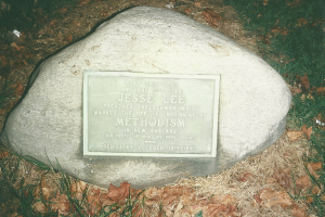 Ein großer Felsen mit einer Tafel, auf der "Jesse Lee Methodism" steht, in einer grasbewachsenen Fläche umgeben von trockenen Blättern und Gras.