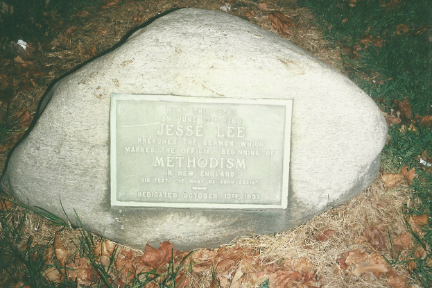 Ein großer Felsen mit einer Tafel, auf der "Jesse Lee Methodism" steht, in einer grasbewachsenen Fläche umgeben von trockenen Blättern und Gras.