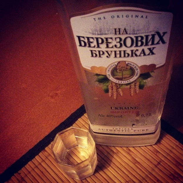 Ein klares Glas mit einer goldenen Flüssigkeit, wahrscheinlich Alkohol, das auf einer dunklen, strukturierten Matte steht.