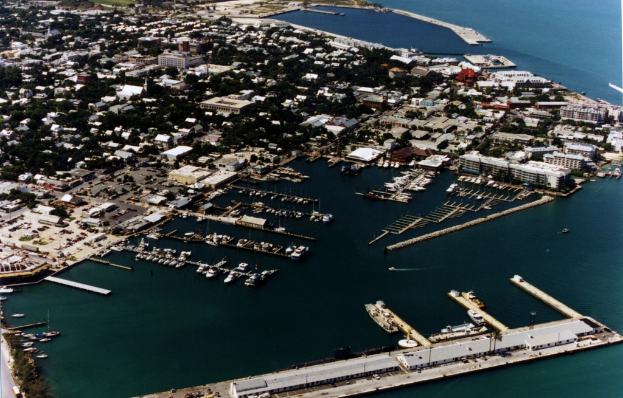 Eine Vogelperspektive einer Stadt mit zahlreichen Gebäuden, Meerwasser und einem Hafen an der Unterseite, mit mehreren Schiffen.
