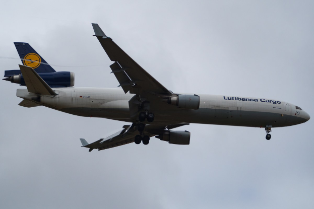 Ein Lufthansa Cargo Boeing 777-300ER im Flug, mit ausgefahrenen Flügeln und laufenden Triebwerken, mit sichtbarem Text auf dem Rumpf gegen einen teilweise bewölkten Himmel.