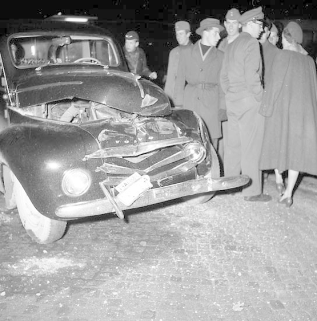Schwarz-Weiß-Bild Eines Schwer Beschädigten Autos An Der Straßen Seite Mit Einer Gruppe Von Menschen, Die Es Begutachten.