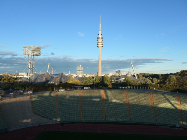 Olympiastadion in Berlin, Deutschland mit dem Fernsehturm im Hintergrund, umgeben von Bäumen, Gebäuden und Lichtern unter einem bewölkten Himmel.