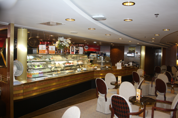 Ein Restaurant-Innenraum mit Tischen und Stühlen, einer Theke mit Blumenvasen, Texttafeln, einem Ventilator und anderen Gegenständen unter einer Decke mit warmer Beleuchtung.