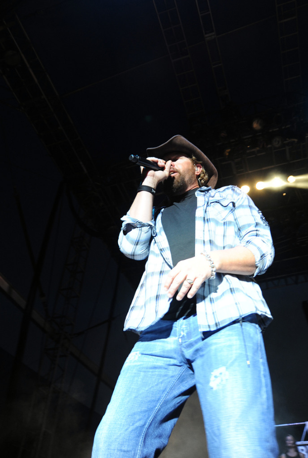 Ein Mann steht auf einer Bühne und singt in ein Mikrofon, während er eine Mütze trägt.