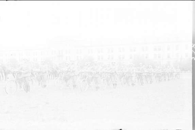 Schwarzes und weißes Foto von Radrennfahrern im Schnee an einem Gebäude vorbei.