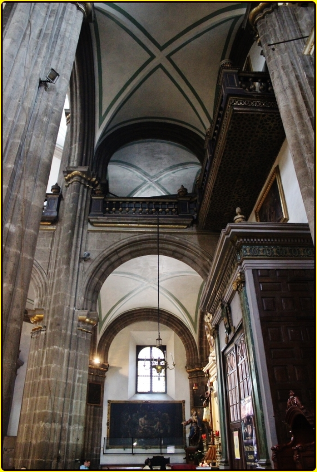 Ein prunkvoller Innenraum eines Palasts mit Schränken, beleuchteten Säulen, Wandskulpturen, einem großen Rahmenbild und einer herabhängenden Lampe von der Decke.