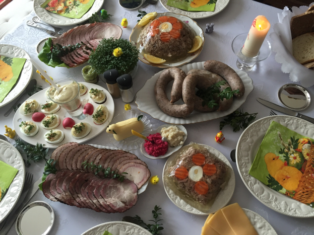 Ein lang gedeckter Tisch mit verschiedenen Gerichten, Besteck, Gläsern, Kerzen und Stühlen, der auf ein traditionelles deutsches Osteressen hinweist.