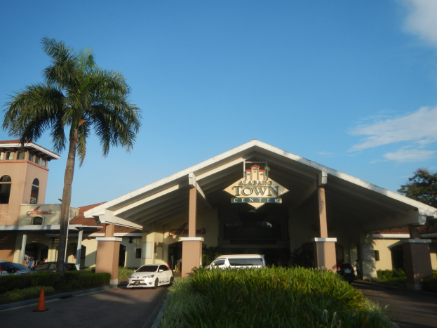 Einfahrt zu einem Resort mit Palmen vorne, umgeben von Gebäuden, Fahrzeugen auf der Straße, Verkehrskegeln, Büschen, Bäumen und einem bewölkten Himmel im Hintergrund.