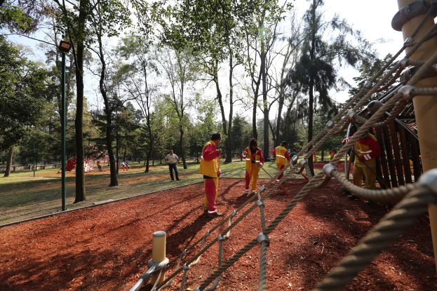 Menschen, die einen Seilparcours in einem Park mit Bäumen im Hintergrund und einer Stange mit Seilen auf der rechten Seite absolvieren.