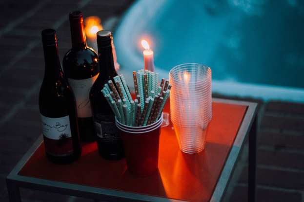 Ein Tisch am Swimmingpool mit zwei Weinflaschen, einer Kerze, Gläsern und Strohhalmen, der auf einen Abend am Pool hinweist.