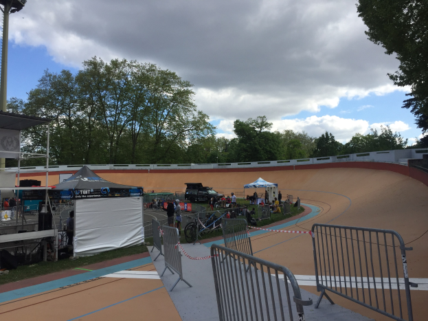 Eine Gruppe von Radfahrern auf einer Schmutzspur bei den UCI BMX-Weltmeisterschaften 2018, mit Zelten, Fahrzeugen und Bäumen im Hintergrund.