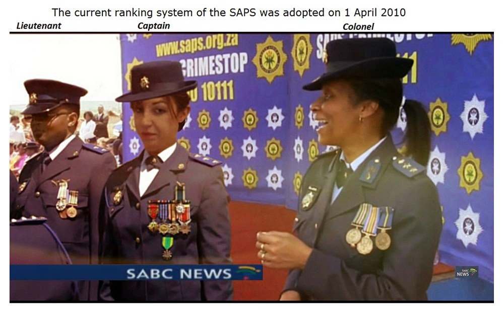 Gruppe von Menschen in Uniformen und Hüten, die mit einem Banner stehen, mit Text oben und unten, der besagt "Das aktuelle Ranglistensystem der SAP wurde am 1. April 2010 übernommen."