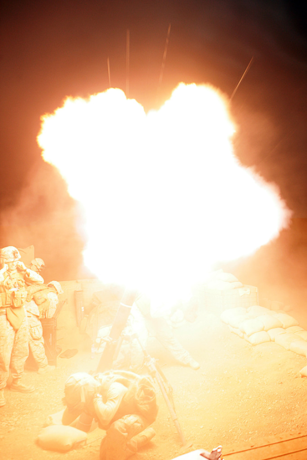 Mehrere Personen in Uniform und Helmen befinden sich auf einem Gelände mit Taschen, mit einem Feuer in der Mitte der Szene.