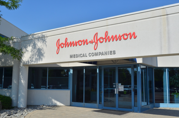 Außenansicht des Johnson & Johnson Medical Companies-Gebäudes mit Glaswänden, Text an der Fassade, Steinen, Pflanzen und einem Baum auf der linken Seite, unter einem klaren blauen Himmel.