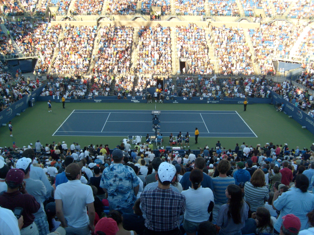 Große Menschenmenge in einem Stadion bei einem Tennisspiel mit Spielern auf dem Platz und Zuschauern in den Rängen.