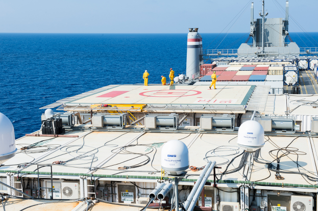 Eine Gruppe von Menschen steht auf einem großen Schiff im Meer, umgeben von Containern, Polen und Drähten, mit dem Himmel im Hintergrund, als Teil eines Offshore-Windparks.