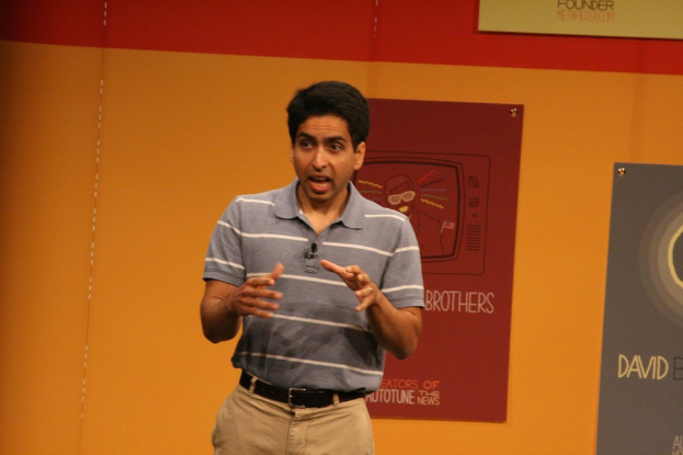 Ein Mann steht auf der Bühne und spricht vor einer Wand mit Postern.