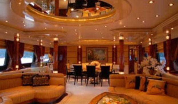 Ein Hotellobby mit Sofas, Stühlen, Tischen und Blumenarrangements im Vordergrund, Fenster mit Vorhängen und Lampen auf beiden Seiten, ein gerahmtes Kunstwerk und Deckenleuchten im Hintergrund und ein großer Spiegel oben.