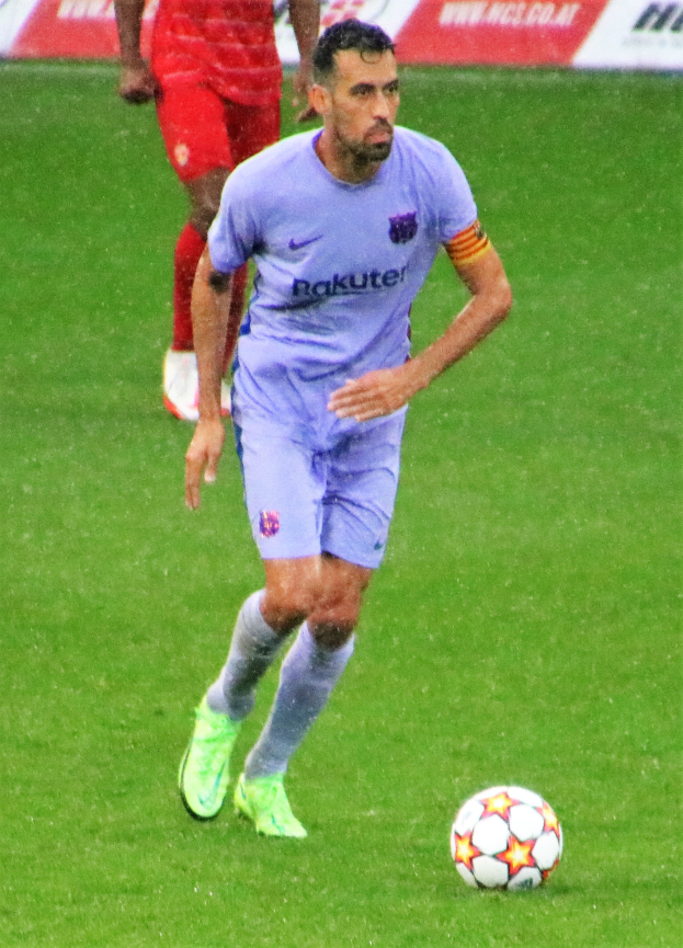 Ein Füßballspieler in einem Sportoutfit und -schuhen ist im Einsatz auf dem Feld, mit einer Texttafel im Hintergrund.