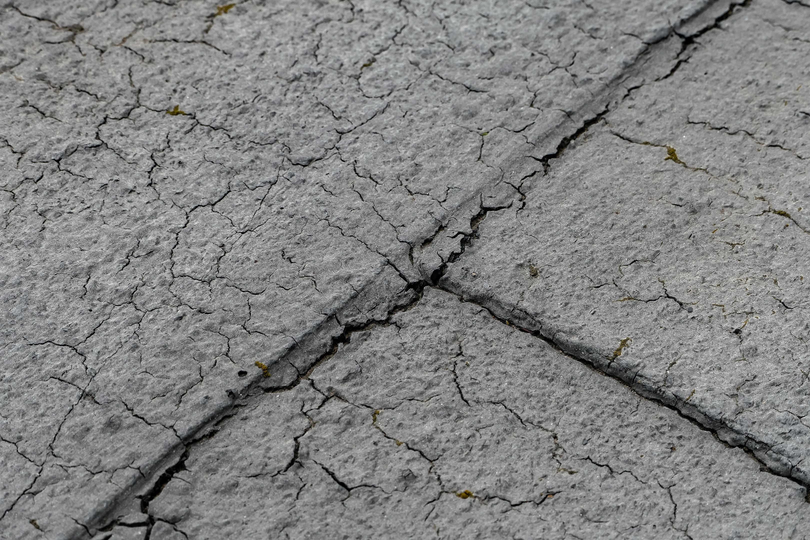 Nahaufnahme einer gebrochenen, verwitterten Straße mit tiefen, breiten Rissen und einer rauen, unebenen Oberfläche.
