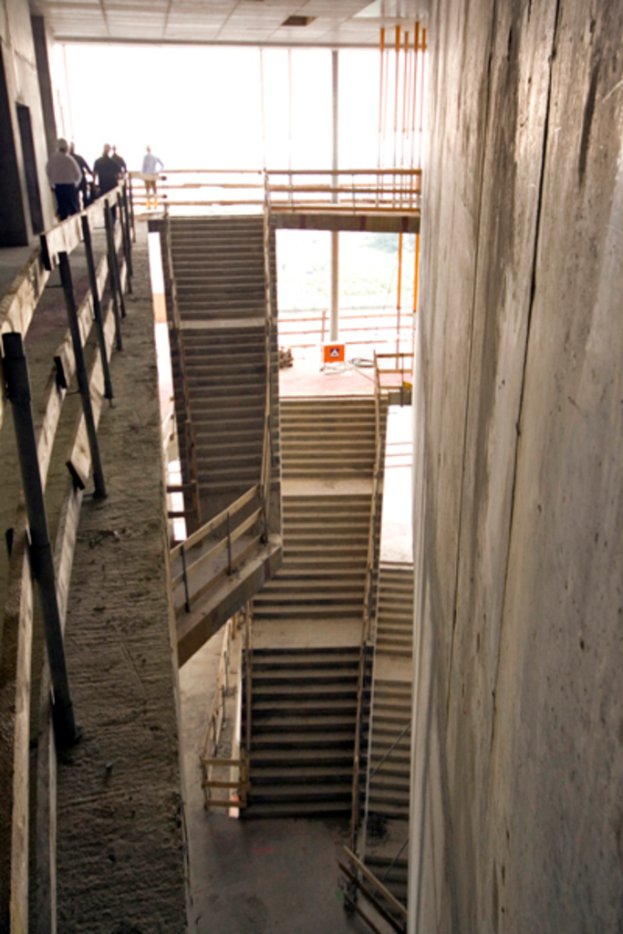 Eine Treppe mit einer Decke oben, einer großen Wand rechts, einem hölzernen Zaun links und einigen Menschen mit Helmen, die neben dem Zaun gehen.