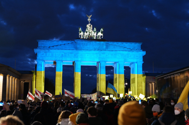 Menschenmenge mit Fahnen und Transparenten vor dem Brandenburger Tor in Berlin, Deutschland, mit einer Schriftrolle auf der rechten Seite.