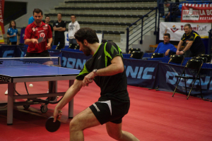 Eine Gruppe von Menschen in verschiedenen Farben, darunter schwarz, weiß und blau, sitzt um einen Tisch mit einem Spiel im Gange, mit Stühlen und einer Treppe im Hintergrund.