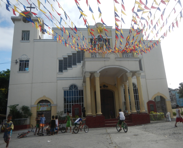 Eine Gruppe von Menschen, die vor einer weißen Kirche mit architektonischen Details wie Fenstern, Säulen, Bögen und einem Kreuz auf Fahrrädern fahren.
