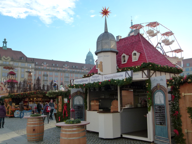 Ein geschäftiger Weihnachtsmarkt in Nürnberg, Deutschland mit Menschen um dekorierte Stände, festliche Lichter, Schmuck, Gebäude, ein großes Rad und einen bewölkten Himmel, mit einer Tafel mit Text auf der rechten Seite.