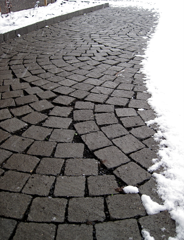 Eine Kopfsteinpflasterstraße mit leichtem Schnee, im Hintergrund ist ein Zaun zu sehen.