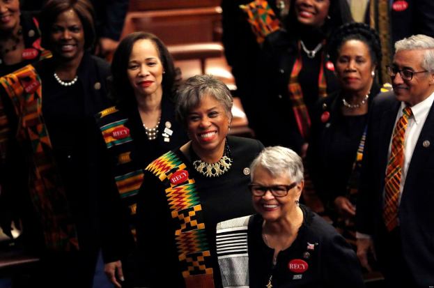Eine Gruppe von Menschen, die zusammen in einem öffentlichen Raum stehen und feiern, wahrscheinlich wegen eines Sieges auf der Democratic National Convention, mit Bänken und einer Wand im Hintergrund.