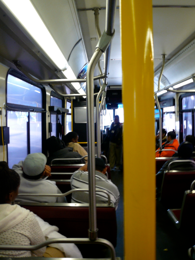 Im Inneren eines Busses sitzen Passagiere auf Bänken mit vertikalen Stangen neben einigen Sitzen.
