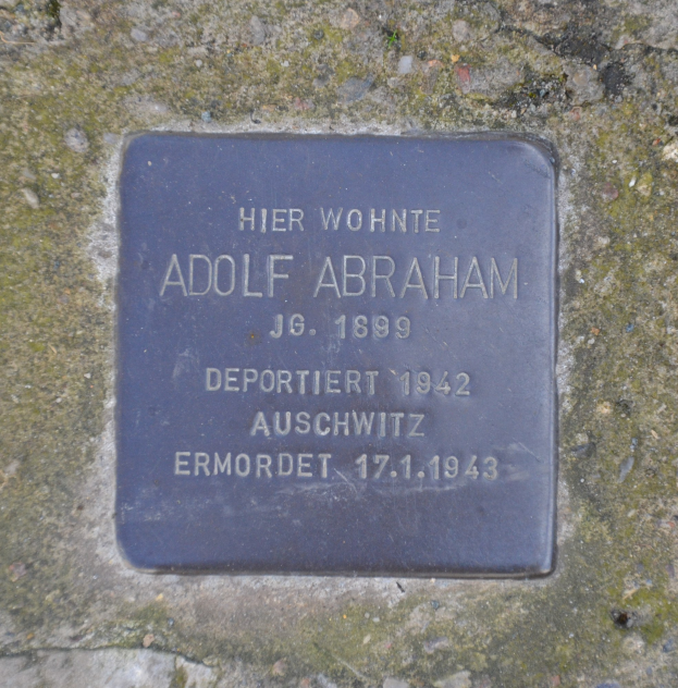 Rechteckige Plakette mit "Adolf Abraham" eingraviert, an einer Steinwand angebracht.
