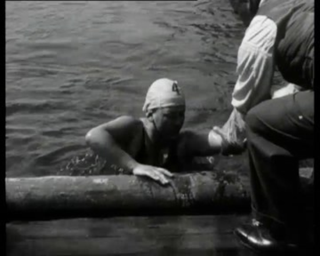 Ein Schwarz-Weiß-Bild eines Mannes in Not im Wasser mit einem Verband am Kopf, umgeben von zwei Personen auf der rechten Seite.