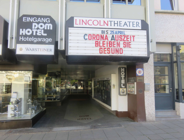Außenansicht des Lincoln Theaters in Berlin, Deutschland, mit Glasfenstern und -türen sowie einer Texttafel und einem Blick auf eine belebte Innenstadtkulisse.