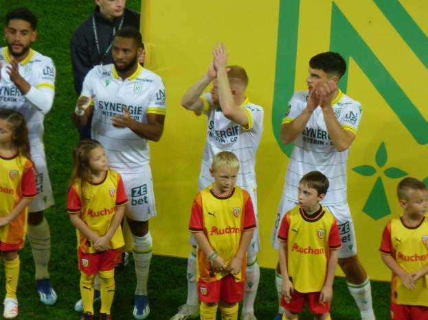 Junge Fußballmannschaft in Uniformen feiert auf einem Ligue-1-Feld, klatscht im Sieg.