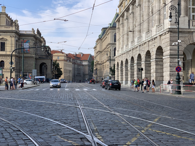 Eine belebte Straße in Prag, Tschechische Republik, mit Fahrzeugen, Füüersonnen, Infrastruktur und Gebäuden unter einem bewölktem Himmel.