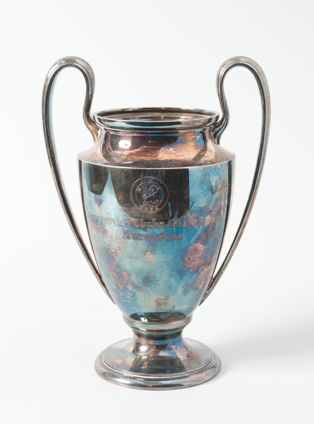 Ein silbern-blauer UEFA-Champions-League-Pokal mit zwei Griffen, darauf eingraviert 'UEFA Champions League', vor einem weißen Hintergrund dargestellt.