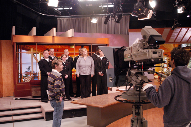 Eine Gruppe von Menschen in einem Fernsehstudio mit einem Kameramann und Deckenlampen im Hintergrund.