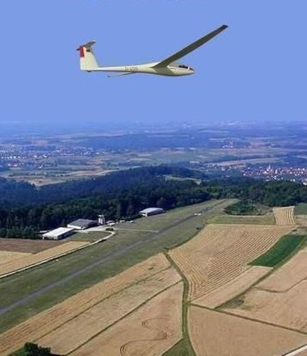 Segelflugzeug über einem Feld mit Bäumen und Gebäuden im Hintergrund, mit Text am oberen Bildrand.