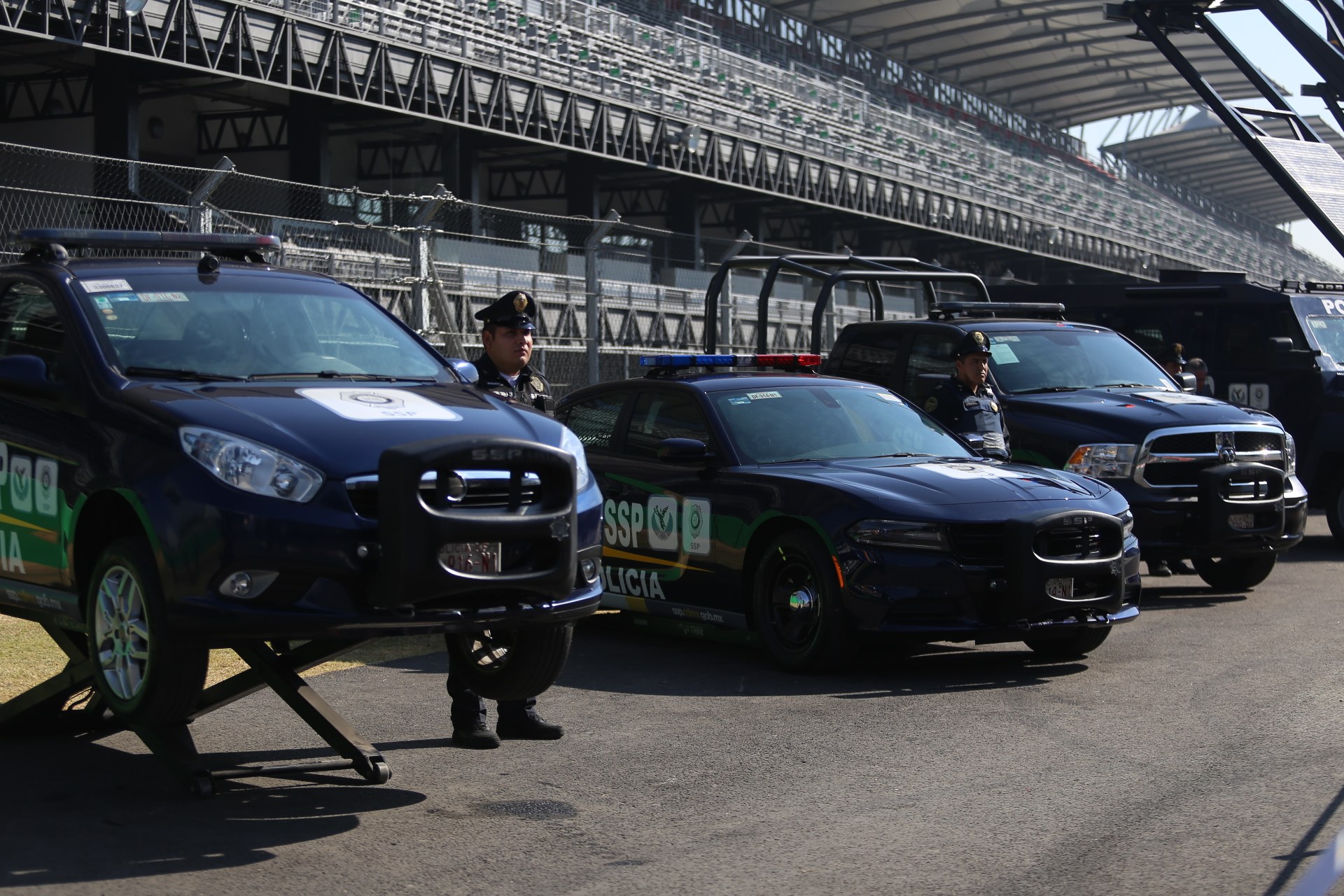 Polizeifahrzeuge vor einer Rennstrecke geparkt, uniformierte Personen, Stadion im Hintergrund und Maschendrahtzaun.