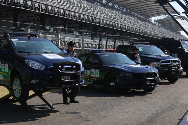 Polizeifahrzeuge vor einer Rennstrecke geparkt, uniformierte Personen, Stadion im Hintergrund und Maschendrahtzaun.