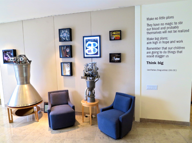 Zwei Sofas stehen nebeneinander, auf dem linken Sofa ein metallisches Objekt und auf der rechten Seite ein Text an der Wand, gerahmte Bilder hängen an der Wand im Hintergrund und ein Boden ist unten sichtbar.